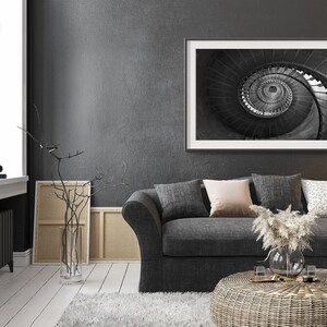 May include: A gray sofa with pillows and a coffee table in a living room with a black and white photo of a spiral staircase hanging on the wall.