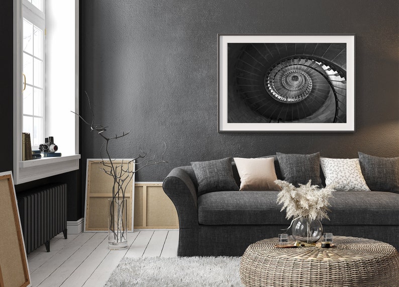 May include: A gray sofa with pillows and a coffee table in a living room with a black and white photo of a spiral staircase hanging on the wall.
