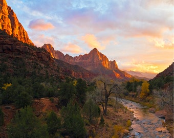 May include: A scenic view of a canyon with red rock cliffs and a river flowing through the valley. The sky is a vibrant orange and pink, creating a beautiful sunset.