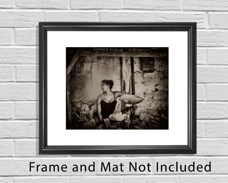May include: A black and white photograph of a woman standing in a doorway with a scale in front of her. The woman is wearing a dark dress and has her hair pulled back. The scale is old and has a wooden base. The photo is taken in a dimly lit room and has a vintage feel.