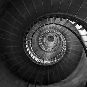 May include: A black and white photo of a spiral staircase winding upwards. The staircase is made of stone and has a metal railing.