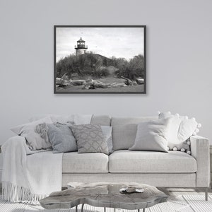 May include: A black and white photograph of a lighthouse on a sandy beach with driftwood in the foreground.