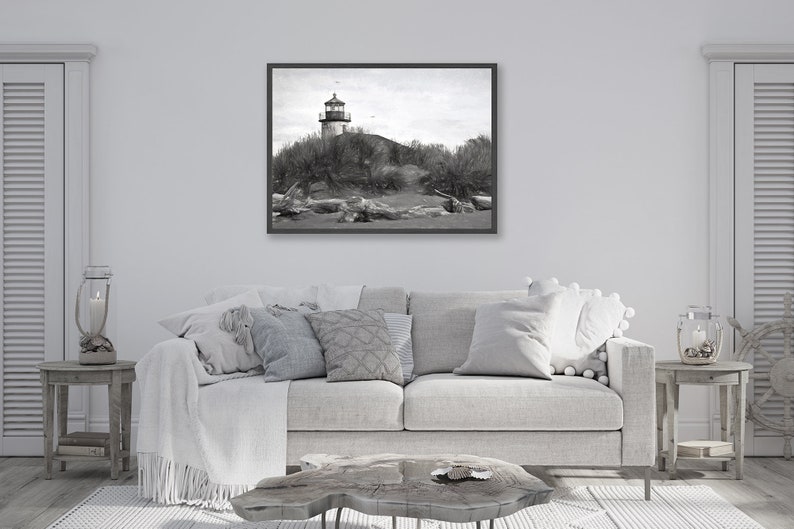 May include: A black and white photograph of a lighthouse on a sandy beach with driftwood in the foreground.
