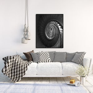 May include: A black and white photograph of a spiral staircase. The photo is framed and hanging on a white wall above a white couch with black and white patterned pillows.