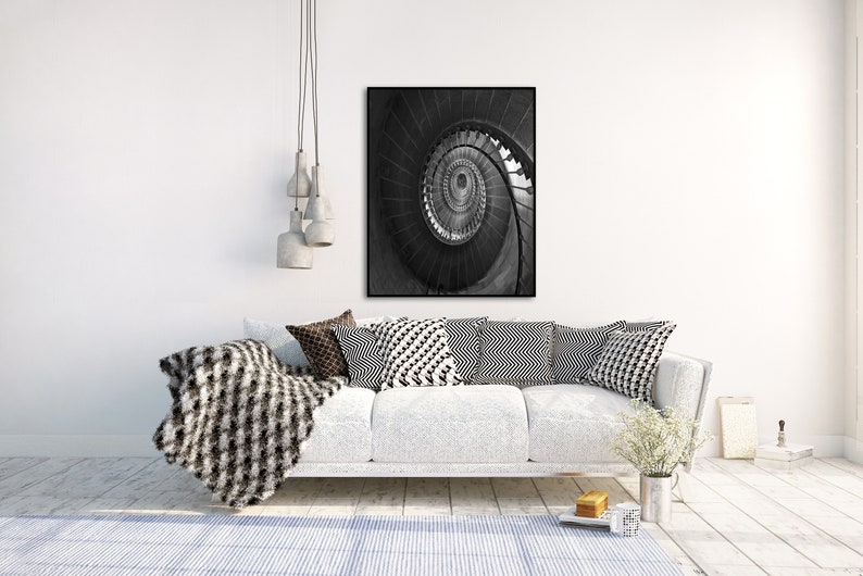 May include: A black and white photograph of a spiral staircase. The photo is framed and hanging on a white wall above a white couch with black and white patterned pillows.
