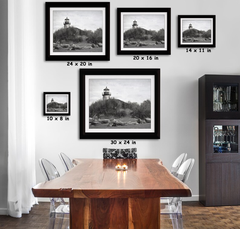 May include: A black and white photograph of a lighthouse on a small island. The lighthouse is tall and slender, with a white tower and a black roof. The island is covered in trees and bushes. The photo is framed in a black frame and is available in various sizes: 10 x 8 inches, 14 x 11 inches, 20 x 16 inches, 24 x 20 inches, and 30 x 24 inches.