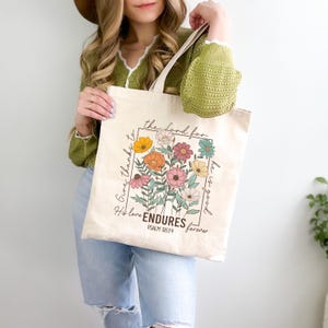 May include: A beige tote bag with a floral design and the text "Give thanks to the Lord for he is good. His love ENDURES forever. Psalm 118:24"