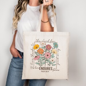 May include: A white canvas tote bag with a floral design and the text "Give thanks to the Lord for he is good. His love ENDURES forever. PSALM 118:24"