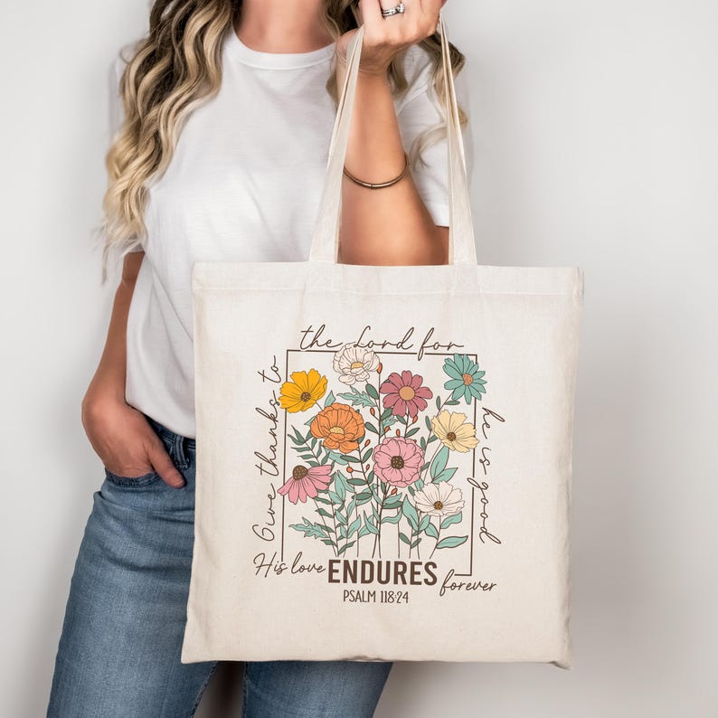 May include: A white canvas tote bag with a floral design and the text "Give thanks to the Lord for he is good. His love ENDURES forever. PSALM 118:24"