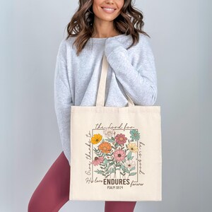 May include: A white canvas tote bag with a floral design and the text "Give thanks to the Lord for he is good. His love ENDURES forever. Psalm 118:24".