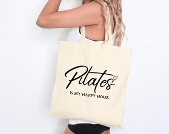 May include: A white canvas tote bag with black text that reads "Pilates is my happy hour" and a small heart symbol.