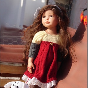 Puede incluir: Una muñeca con el pelo largo y castaño que lleva un vestido de punto rojo, blanco y gris con un ribete de encaje blanco. La muñeca sostiene un cachorro dálmata blanco y negro.