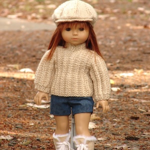 Puede incluir: Una muñeca con un suéter de punto beige, pantalones cortos de mezclilla azul y una gorra de golf beige. La muñeca tiene el pelo largo y rojo y lleva botas blancas.