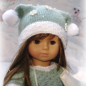 Peut inclure: Une poupée portant un bonnet en tricot bleu clair et blanc avec des pompons blancs et un pull bleu clair avec des bordures blanches. La poupée tient un patin à glace blanc.