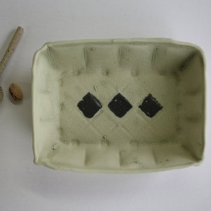Puede incluir: Un plato rectangular de cerámica verde claro con tres formas de diamantes negros pintadas en el fondo.