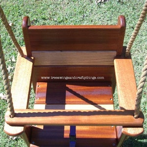 May include: A wooden baby swing with a natural finish, featuring a seat, backrest, and armrests. The swing is suspended by thick, beige ropes. The text "www.treeswingsandcraftythings.com" is visible on the swing.
