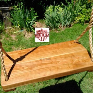 May include: A wooden swing with a natural finish, suspended by thick, woven rope. The swing seat is rectangular and appears to be made of solid wood. The image includes a "Made in USA" logo.