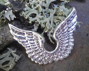 May include: Silver-toned metal angel wings charm with a detailed, feathery design. The wings are joined at the base, creating a U-shape.