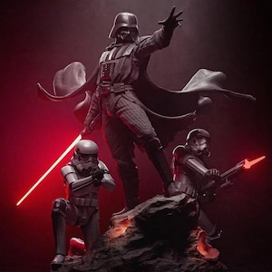 May include: A detailed statue of Darth Vader with a red lightsaber, and two Stormtroopers. The figures are posed on a rocky surface, with a dark red background. A collectible item.