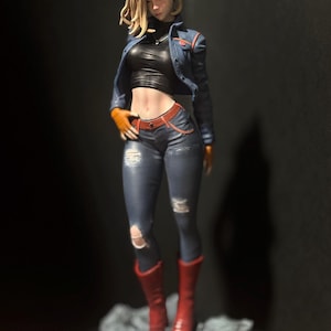 May include: A detailed figurine of a female character with blonde hair, wearing a blue denim jacket, a black tank top, blue jeans with rips, and red boots. The figurine is standing on a gray base.