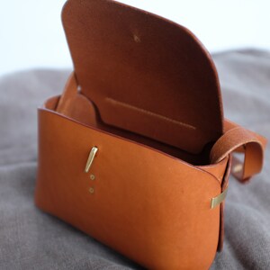 May include: A brown leather satchel bag with a brass clasp and a strap. The bag is open and the inside is visible.