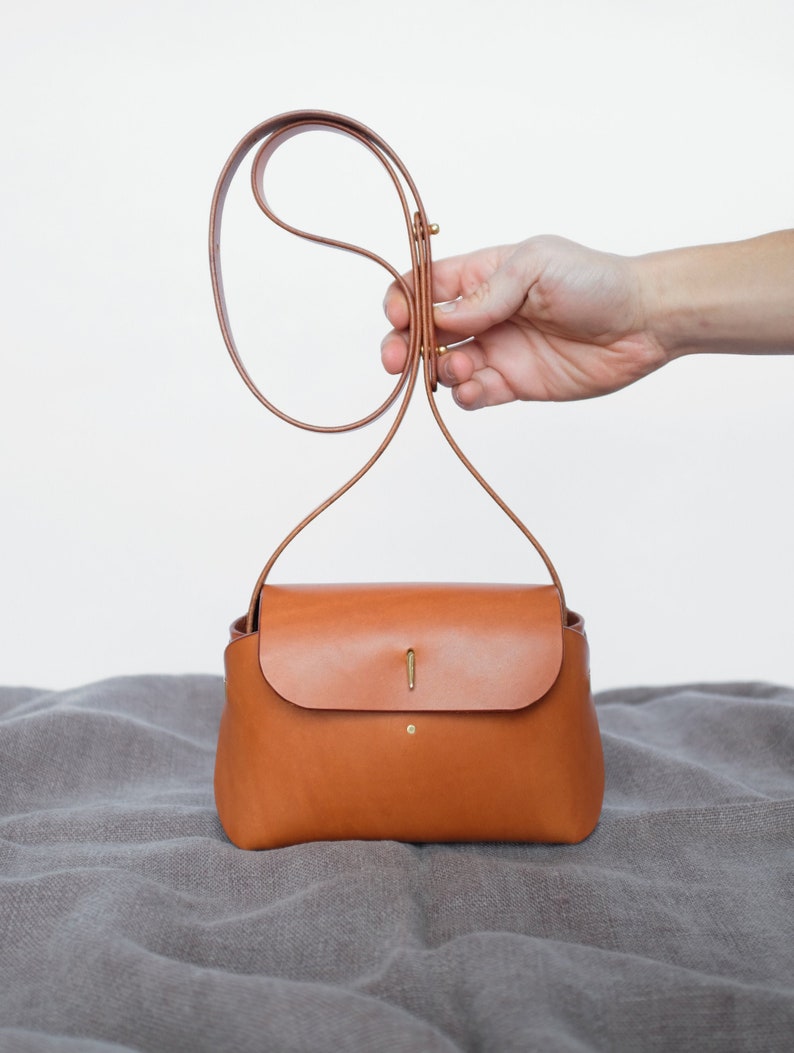 May include: A small, brown leather crossbody bag with a flap closure and a gold metal clasp. The bag has a long, adjustable strap.