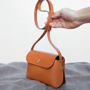 May include: A small, brown leather crossbody bag with a gold clasp and a long strap.