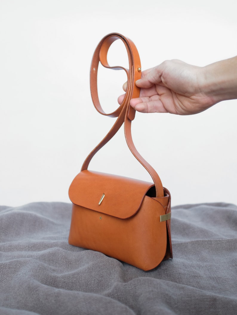 May include: A small, brown leather crossbody bag with a gold clasp and a long strap.
