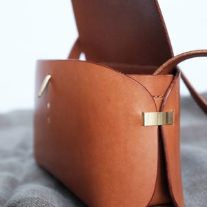 May include: A brown leather crossbody bag with a flap closure and a gold metal clasp. The bag is open and the inside is visible.