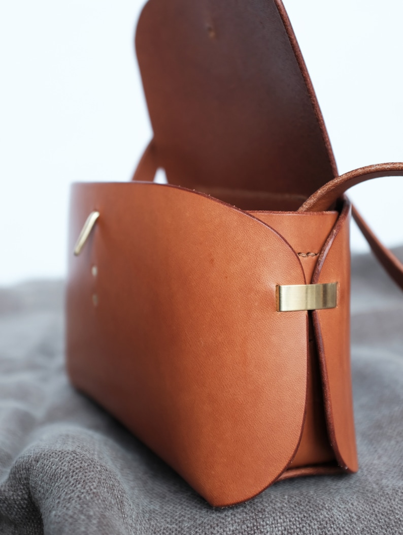 May include: A brown leather crossbody bag with a flap closure and a gold metal clasp. The bag is open and the inside is visible.