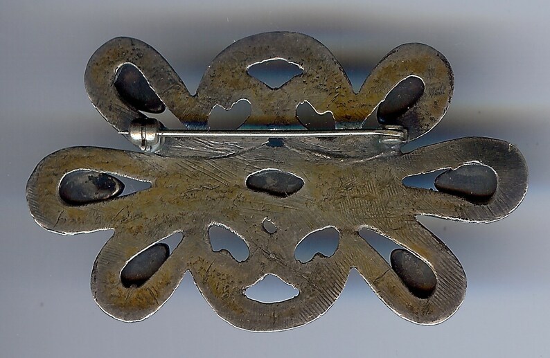 May include: Silver tone brooch with a floral design. The brooch has a pin and catch closure on the back.