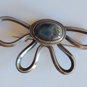 Puede incluir: Un broche de plata con forma de flor con una piedra preciosa azul oscuro en el centro.