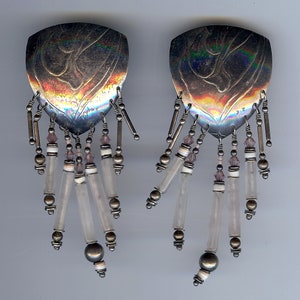 May include: A pair of silver earrings with a teardrop-shaped design and dangling clear and pink beads.