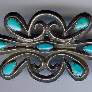 May include: A silver brooch with a stylized design and turquoise stones.