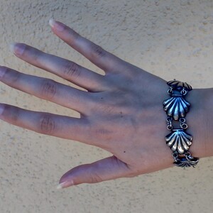 May include: A silver bracelet with a chain and multiple shell-shaped charms. The bracelet is on a person's wrist.