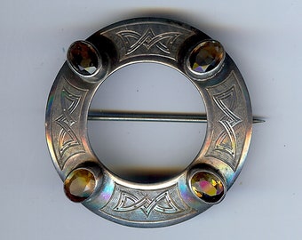 May include: A silver circular brooch with a Celtic knot design and four amber-colored gemstones.