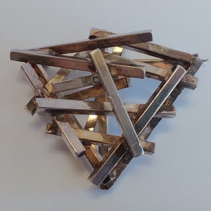May include: A silver-coloured metal brooch with a geometric design. The brooch features numerous rectangular bars arranged in a seemingly random, yet cohesive, pattern. The metal has a slightly tarnished appearance, adding character.