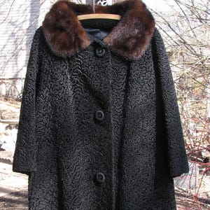May include: A black, curly-textured coat with a brown fur collar. The coat has a button closure and is hanging on a wooden post.
