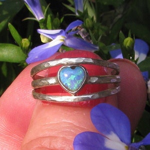 May include: A silver ring with three bands and a heart-shaped opal gemstone. The opal is a light blue color with green and white flashes.