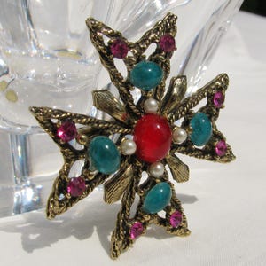 Puede incluir: Broche vintage en forma de cruz dorada. La broche presenta una piedra roja central, piedras de color turquesa y pedrer&iacute;a rosa. Peque&ntilde;as perlas de imitaci&oacute;n y detalles en metal dorado completan el dise&ntilde;o. Un accesorio decorativo.
