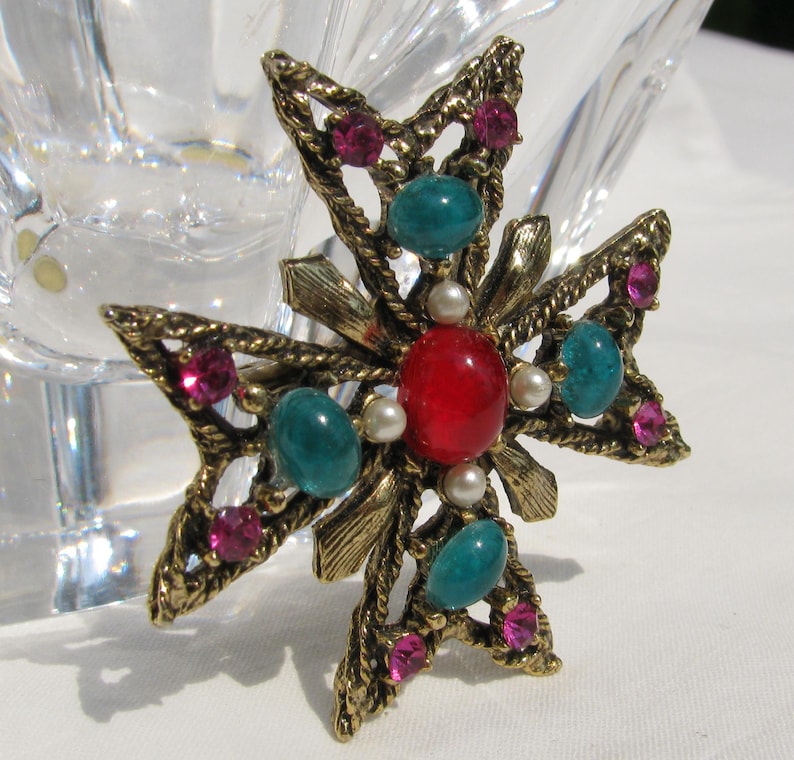 Puede incluir: Broche vintage en forma de cruz dorada. La broche presenta una piedra roja central, piedras de color turquesa y pedrer&iacute;a rosa. Peque&ntilde;as perlas de imitaci&oacute;n y detalles en metal dorado completan el dise&ntilde;o. Un accesorio decorativo.