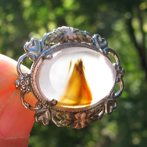May include: A silver-toned pendant with an oval-shaped agate stone. The agate has a white background with a brown and orange swirl pattern.