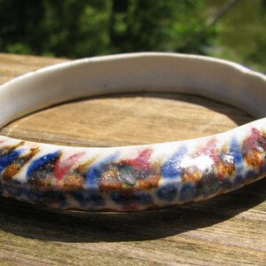 May include: A white ceramic bangle bracelet with a blue, brown, and pink abstract pattern.