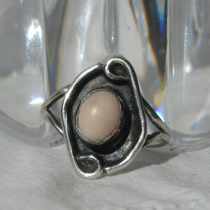 May include: A silver ring with a delicate design featuring a pale pink oval gemstone.