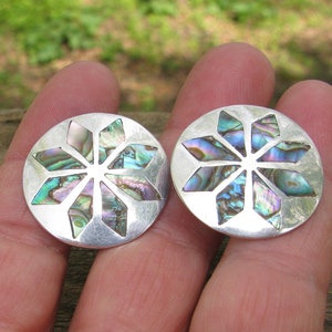 Puede incluir: Un par de pendientes de plata con un dise&ntilde;o circular que presenta un patr&oacute;n de estrella en forma de estrella hecho de concha de abul&oacute;n iridiscente.