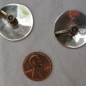 Puede incluir: Un par de pendientes de plata con un peque&ntilde;o dise&ntilde;o de flor. Los pendientes son aproximadamente del tama&ntilde;o de una moneda de un c&eacute;ntimo de euro.