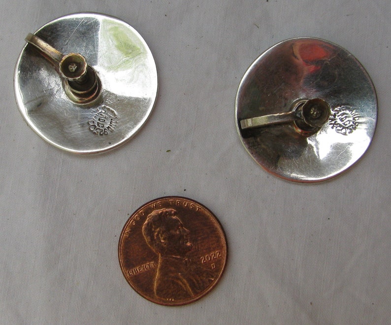 Puede incluir: Un par de pendientes de plata con un peque&ntilde;o dise&ntilde;o de flor. Los pendientes son aproximadamente del tama&ntilde;o de una moneda de un c&eacute;ntimo de euro.