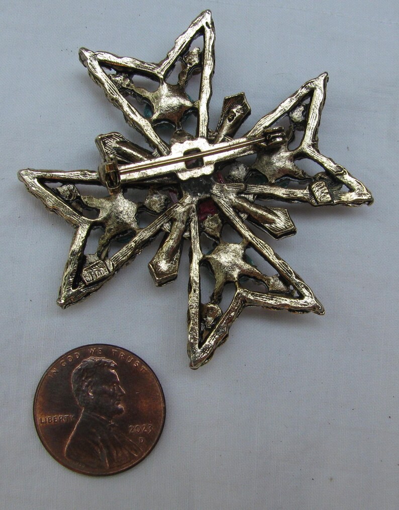 Puede incluir: Broche vintage dorado en forma de estrella con cierre de alfiler. El broche presenta un dise&ntilde;o calado con peque&ntilde;os acentos coloridos. Una moneda est&aacute; al lado del broche para comparar el tama&ntilde;o.