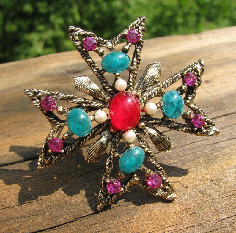 Puede incluir: Broche vintage dorado en forma de cruz, adornado con piedras preciosas rojas, turquesas y rosas, y peque&ntilde;as perlas blancas. El broche tiene un dise&ntilde;o detallado y texturizado con una piedra roja central y piedras turquesas en cada brazo.