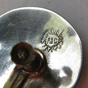 Puede incluir: Primer plano de un objeto de metal plateado con un sello circular que dice "STERLING 925 MEXICO".